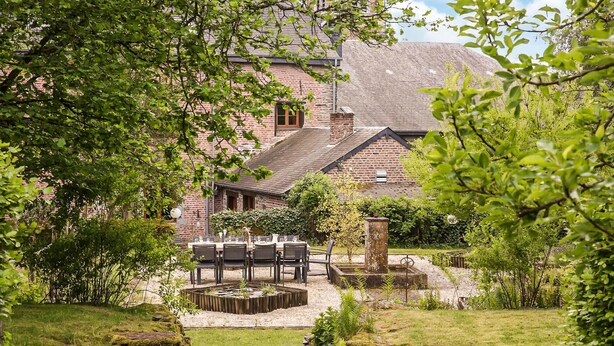 A rustic stone building with a brick exterior, surrounded by lush greenery and a small outdoor seating area with tables and chairs. - Amazing home in Gedinne with sauna (Gedinne)