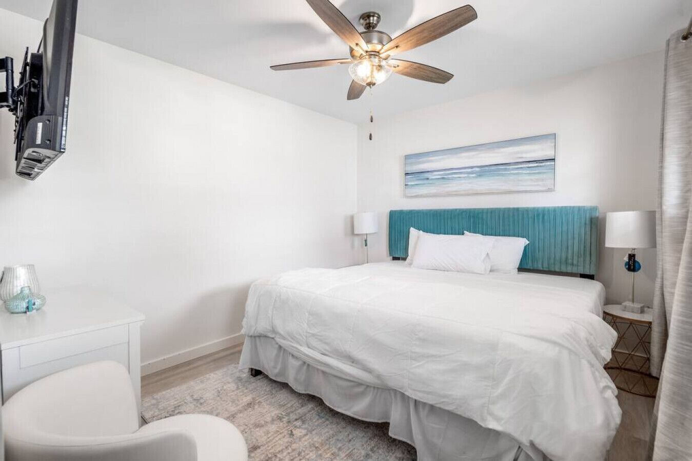 Une chambre d’hôtel avec un lit, un ventilateur de plafond, un téléviseur fixé au mur et un tableau au-dessus du lit.