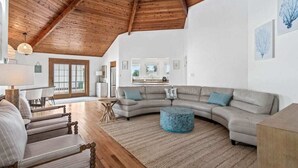 A spacious living room with a large L-shaped sectional sofa, a round ottoman, and a wooden coffee table.