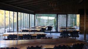 A spacious indoor dining area with large wooden tables and chairs, large windows offering a view of the outdoors. - Pagen Bungalov (Hopa)