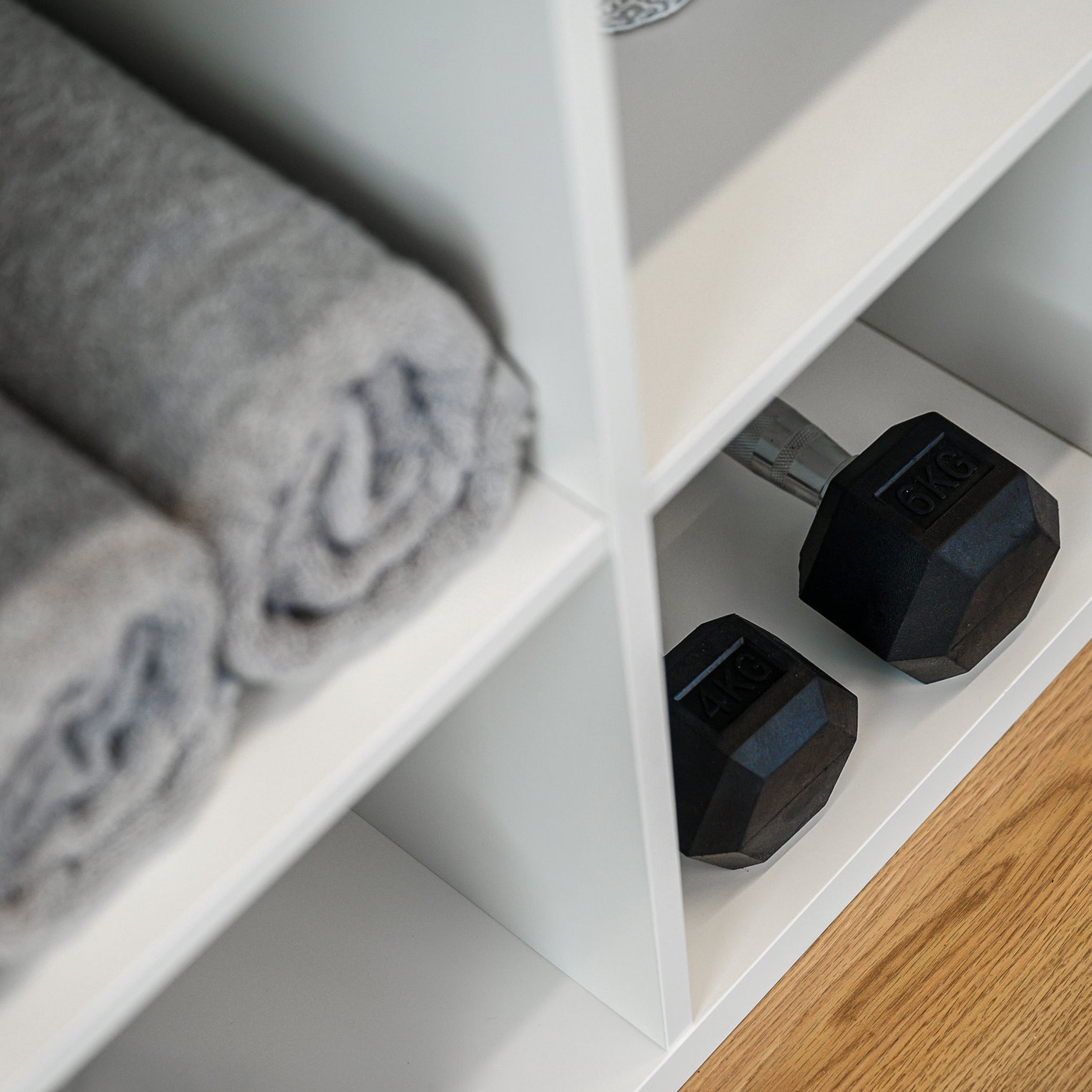 A white shelf with two black dumbbells and a rolled-up towel.
