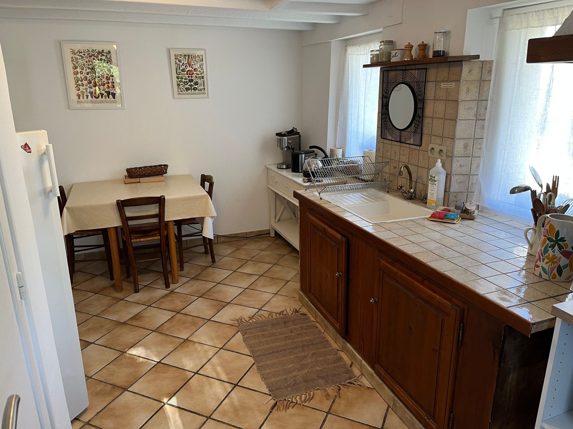 A kitchen with a dining table, chairs, a sink, and a window with curtains.