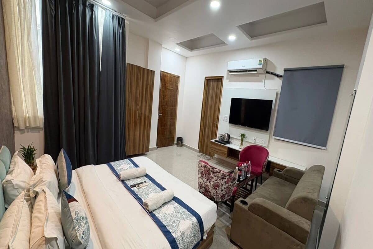 A modern hotel room with a large bed, a sofa, a TV, and an air conditioning unit.