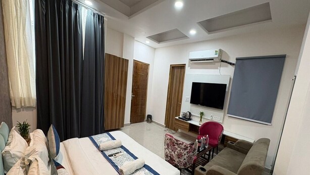 A modern hotel room with a large bed, a sofa, a TV, and an air conditioning unit. - Radiant Blu Hotel (Noida)