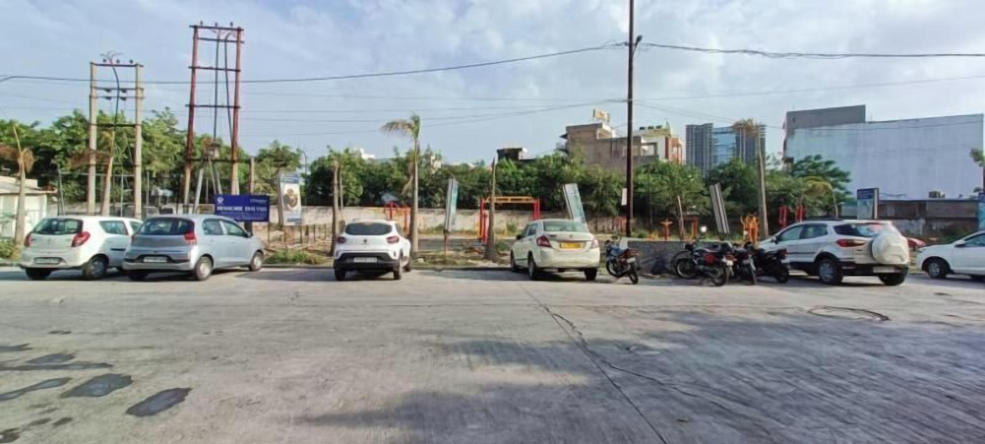 A parking lot with several cars and motorcycles, utility poles, and buildings in the background.