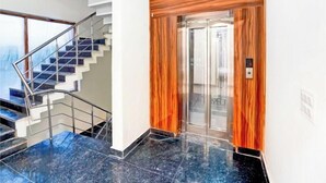 A modern elevator with a wooden panel design, a glass door, and a control panel. - Radiant Blu Hotel (Noida)