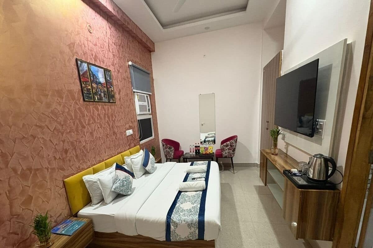 A hotel room with a bed, a TV, a small table with chairs, and a kitchenette area.