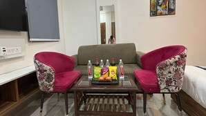 A room with a sofa, two armchairs, a coffee table with snacks, a TV, and artwork on the wall. - Radiant Blu Hotel (Noida)