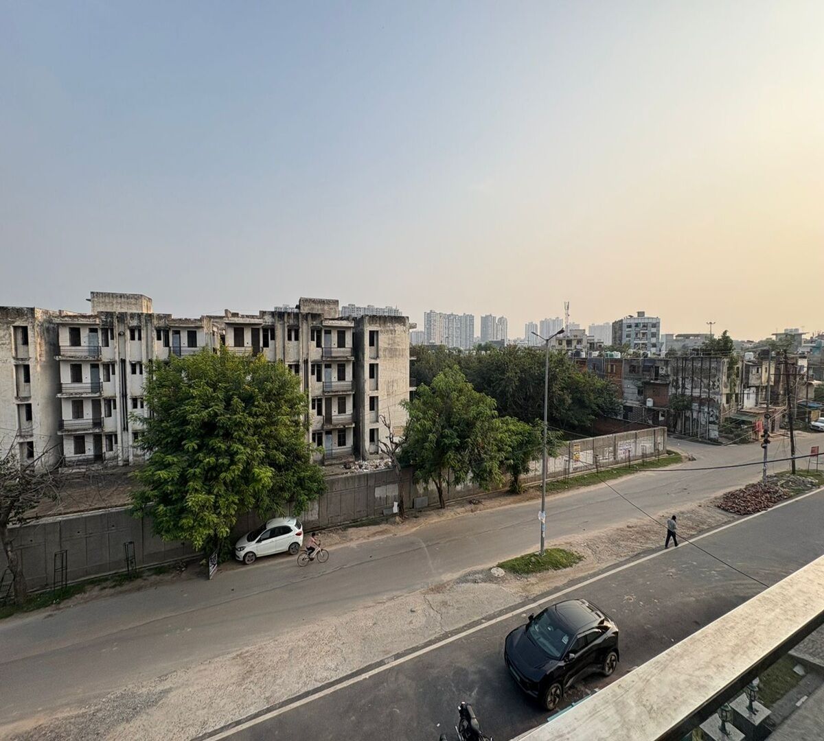 A multi-story residential building with balconies, a paved road, and a few vehicles.