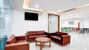A modern lobby with leather sofas, a wooden coffee table, and a flat-screen TV mounted on the wall. - Radiant Blu Hotel (Noida)