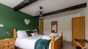 Een slaapkamer met een bed, nachtkastje van hout, groene wanden, een plafondventilator, een spiegel en een houten kledingkast.