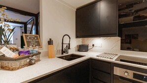 Een moderne keuken met donkere kastjes, een inbouwoven en een spoelbak. Er staat een welkomstbord en een mandje met toiletartikelen op het aanrecht.