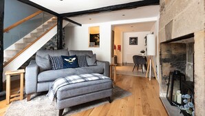 Een moderne woonkamer met een grijze bank, een passend voetenbankje, en een trap naar een hoger niveau.