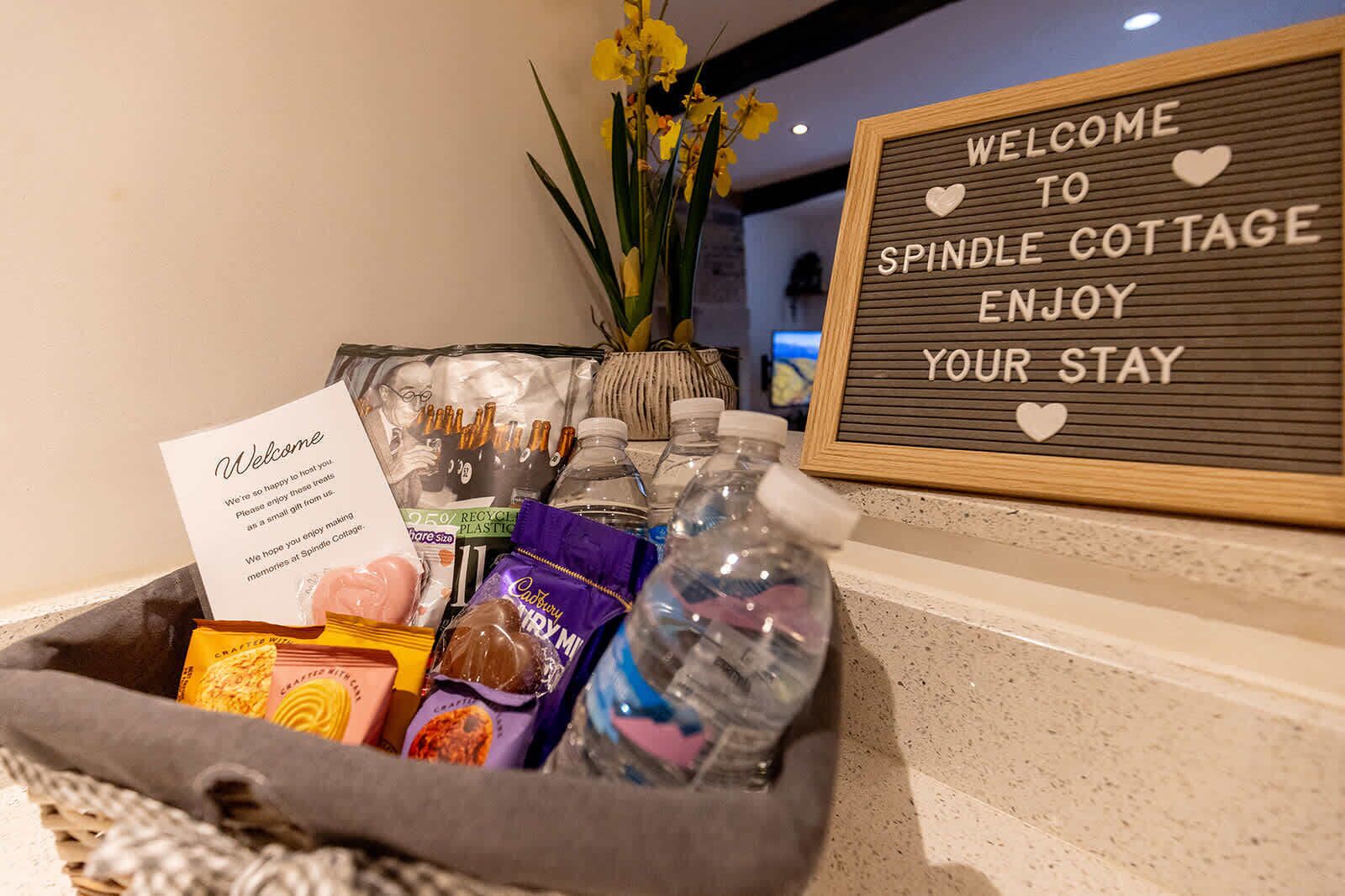 En välkomstskylt vid hotellreceptionen, en korg med hygienartiklar och en vas med gula blommor.