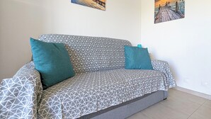 Un salon moderne avec un canapé aux motifs géométriques, des coussins de couleur turquoise et deux tableaux représentant des couchers de soleil, accrochés au mur.