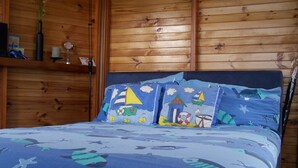 Une chambre avec des lambris en bois, un lit avec une literie bleue ornée de motifs représentant des créatures marines, et une étagère sur laquelle se trouvent un vase et une horloge.