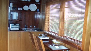 Une cuisine compacte avec des meubles en bois, un grille-pain encastré, un évier et une fenêtre avec des stores.
