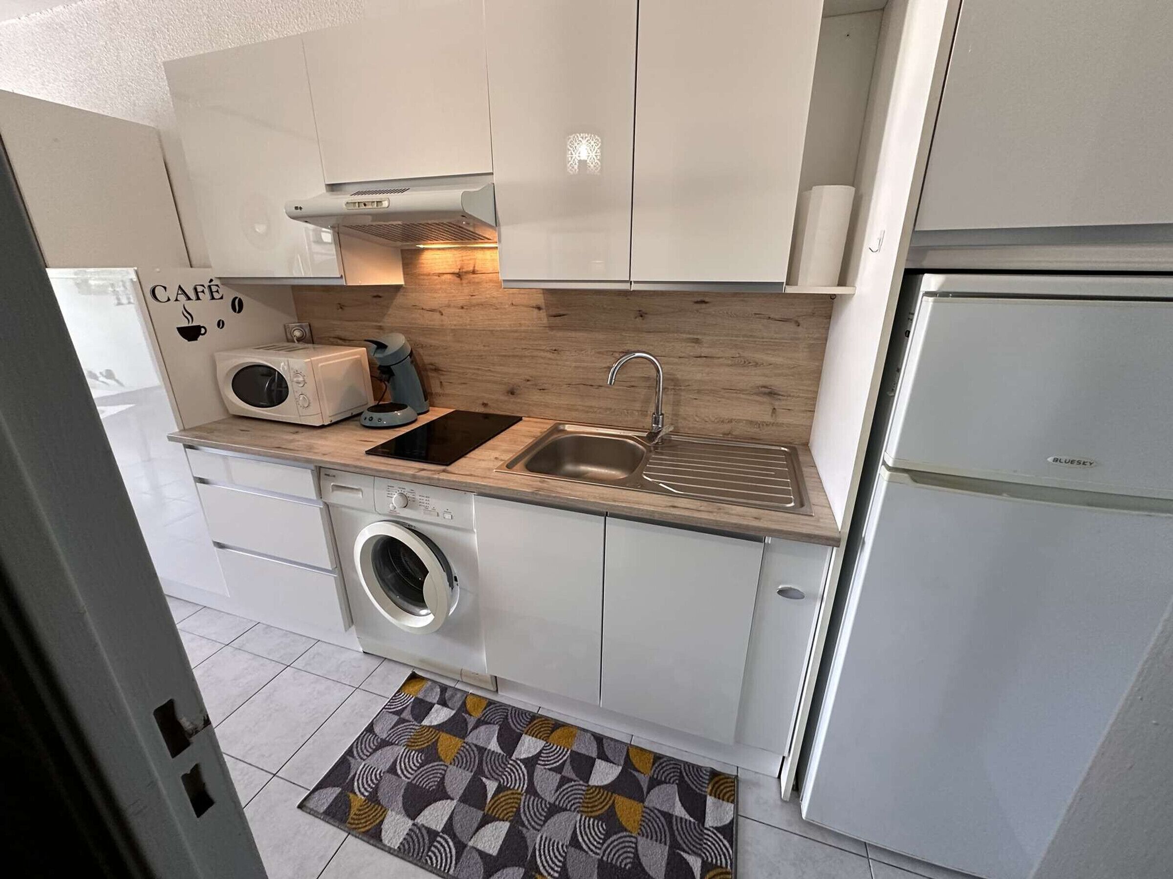 Une cuisine compacte équipée d’un lave-linge, d’un évier, d’un grille-pain et d’une machine à café.
