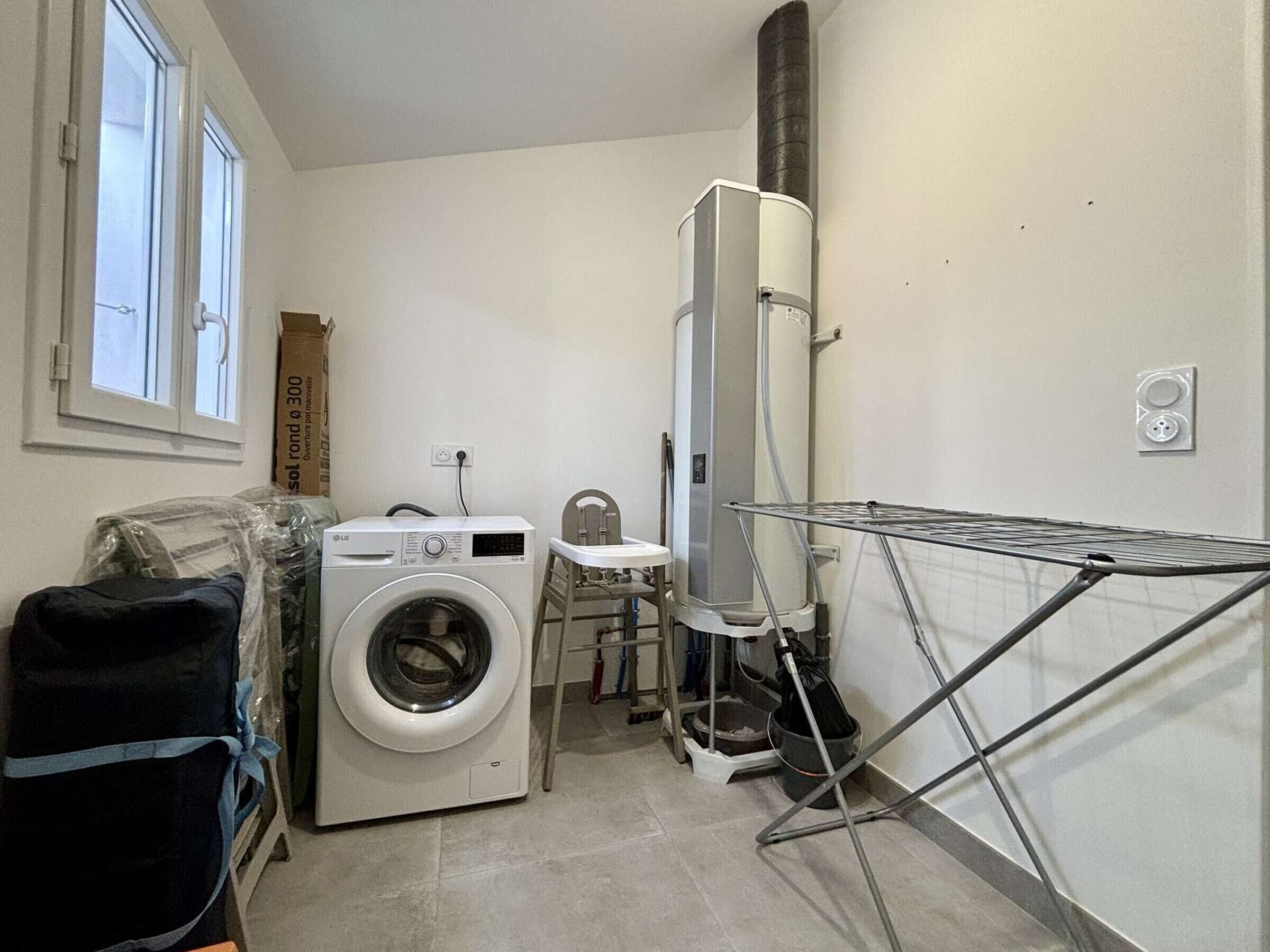 Een wasserette met een voorlader wasmachine, een hoge boiler, een droogrek en een kleine stoel.
