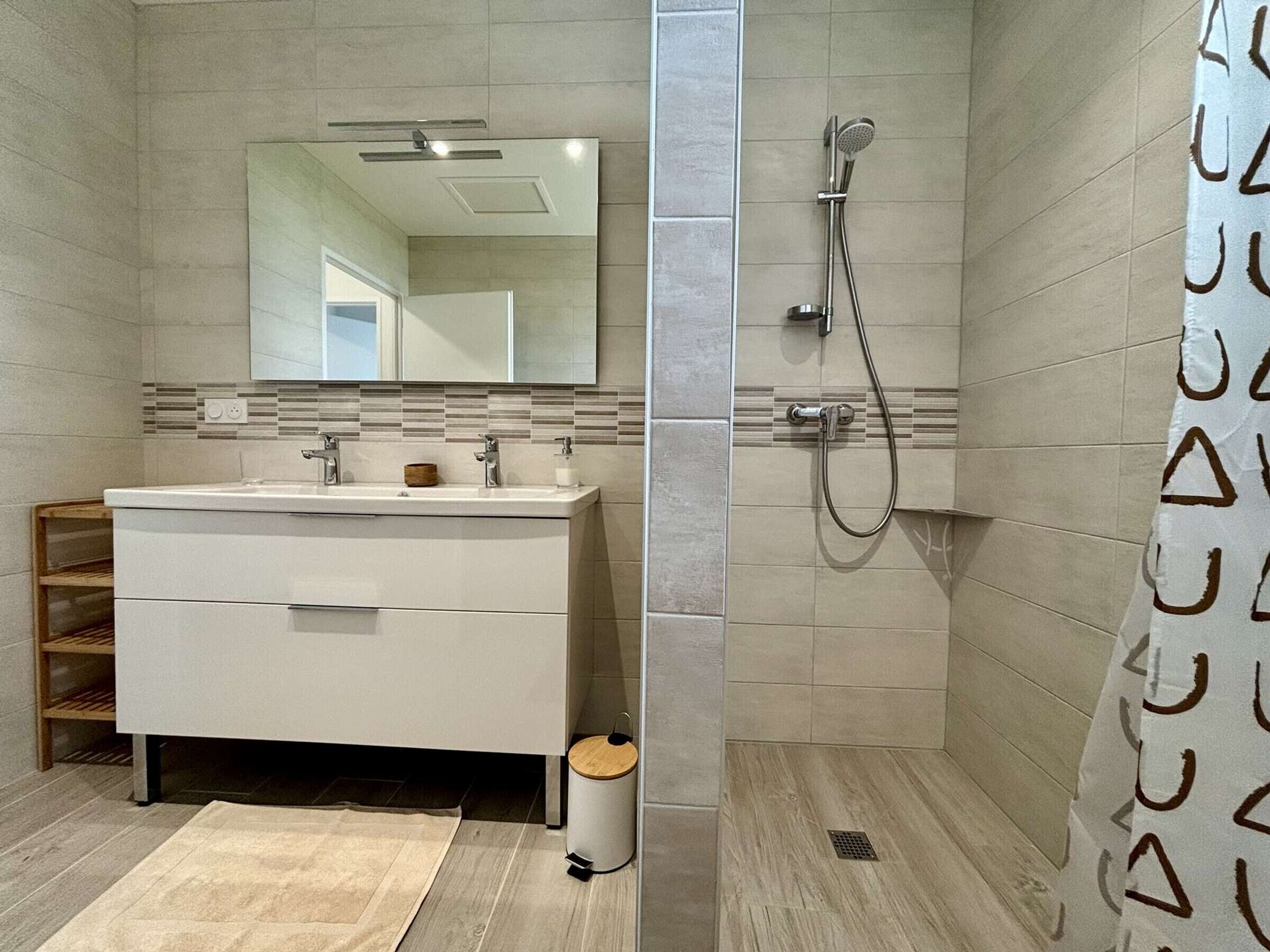 Un bagno moderno con un mobile lavabo bianco, uno specchio, una doccia con soffione a mano e un telo da doccia decorato.
