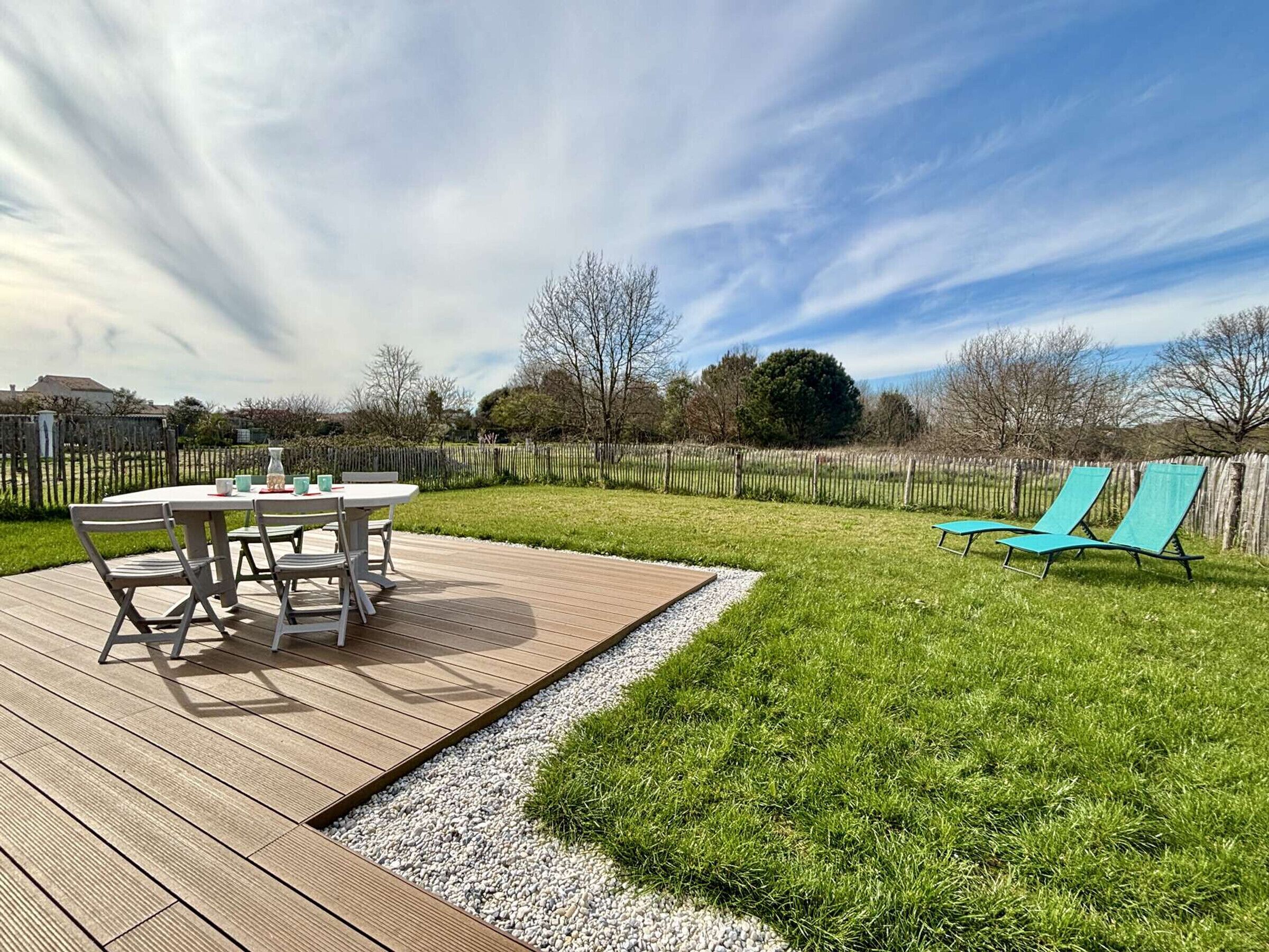 A deck with a table and chairs, a grassy area with a wooden fence, and a clear sky.
