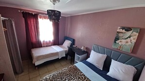 Habitación de hotel con dos camas individuales, un escritorio con silla, un ventilador de techo y un cuadro en la pared.