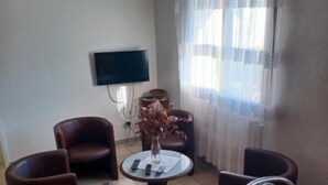 Una sala de estar con un televisor montado en la pared, una mesa redonda con sillas y una ventana con cortinas.