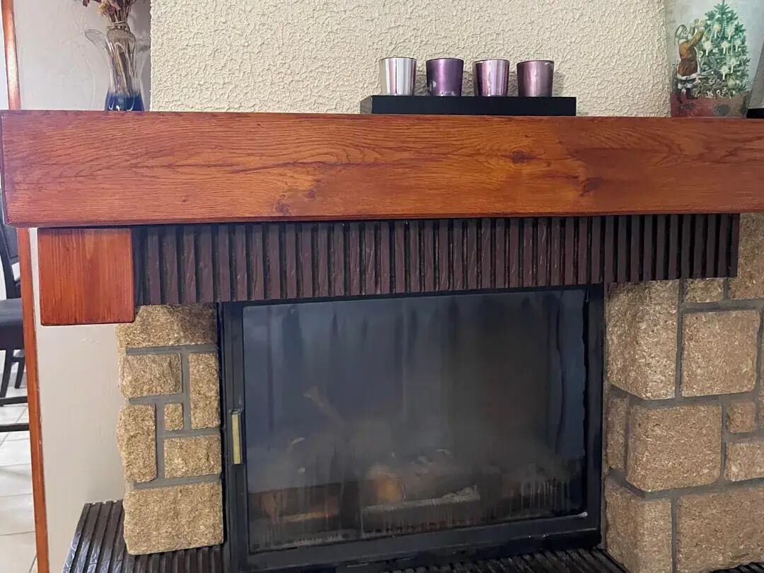 Une cheminée avec un foyer en pierre et une étagère en bois au-dessus.