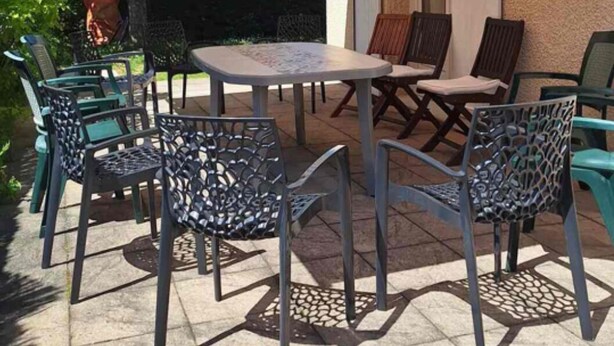 Un patio al aire libre con una mesa y sillas, un toldo a rayas, y un edificio al fondo.