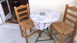 A small round table with a floral tablecloth, two wooden chairs with woven seats, and a green metal base.