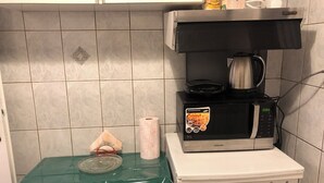 A kitchen with a microwave oven, a gas stove, and a shelf above the stove holding a coffee pot and some items.