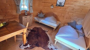 A cozy cabin interior with a wooden dining table, a sofa bed, and a small cabinet. - Pension Edi (Leutasch)