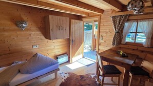 A cozy cabin interior with a bed, a small table, chairs, a heater, and a window with curtains. - Pension Edi (Leutasch)