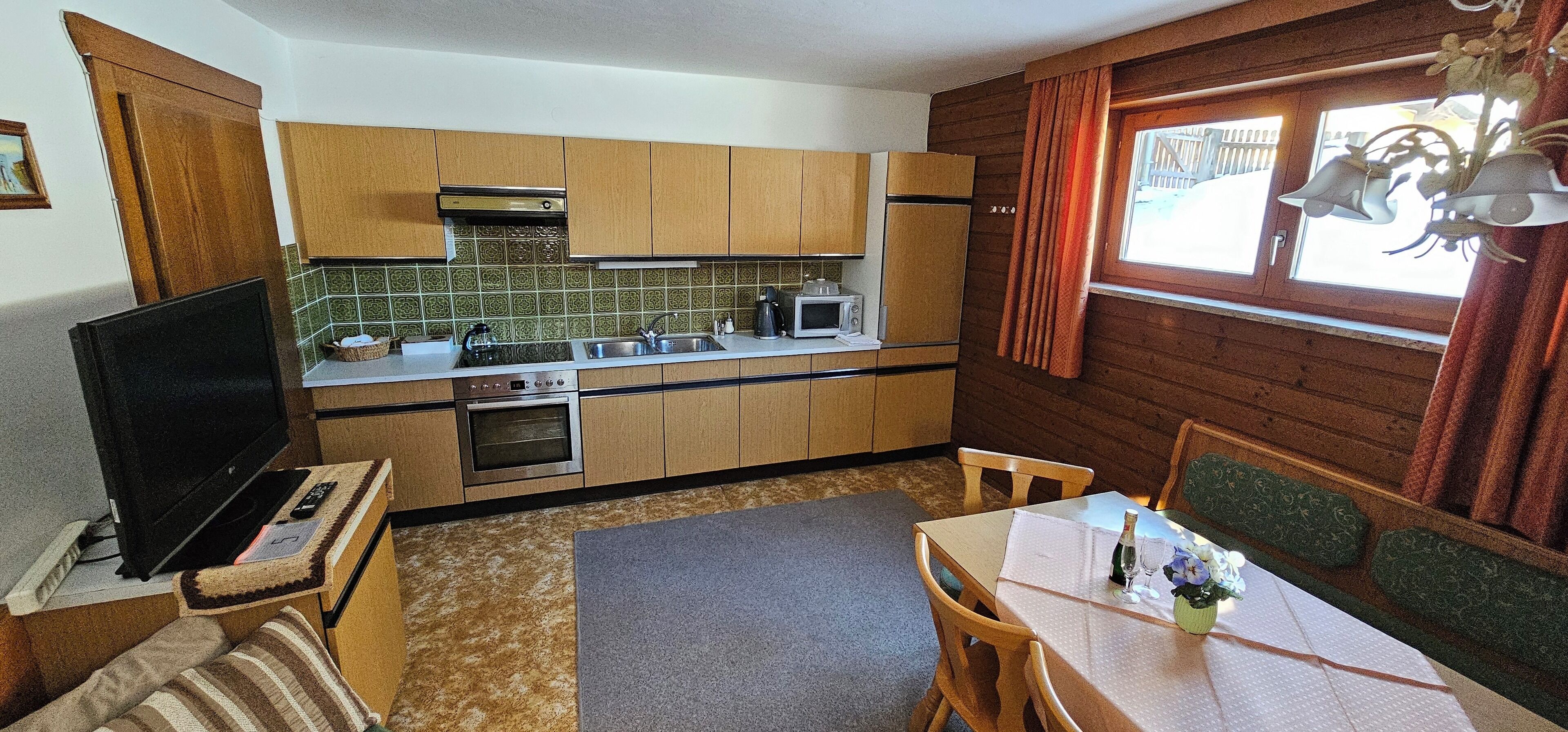 A compact kitchen with wooden cabinets, a microwave, an oven, and a television on a small table.