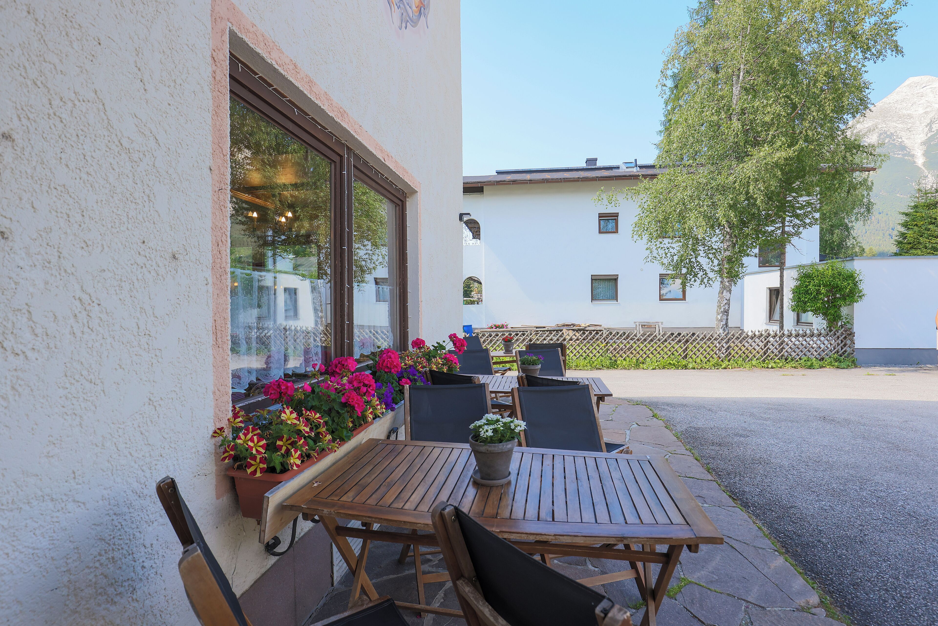 Eine Außenpatio mit Holztischen und -stühlen, Topfpflanzen und Blick auf ein Gebäude im Hintergrund.