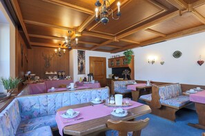 A restaurant with wooden ceiling beams, floral-patterned booths, and a checkered tablecloth. - Pension Edi (Leutasch)