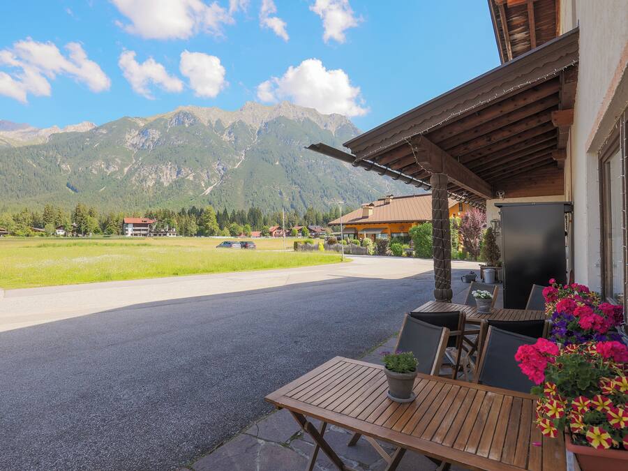 Un tavolo di legno con sedie e piante in vaso su un balcone con vista sulle montagne.