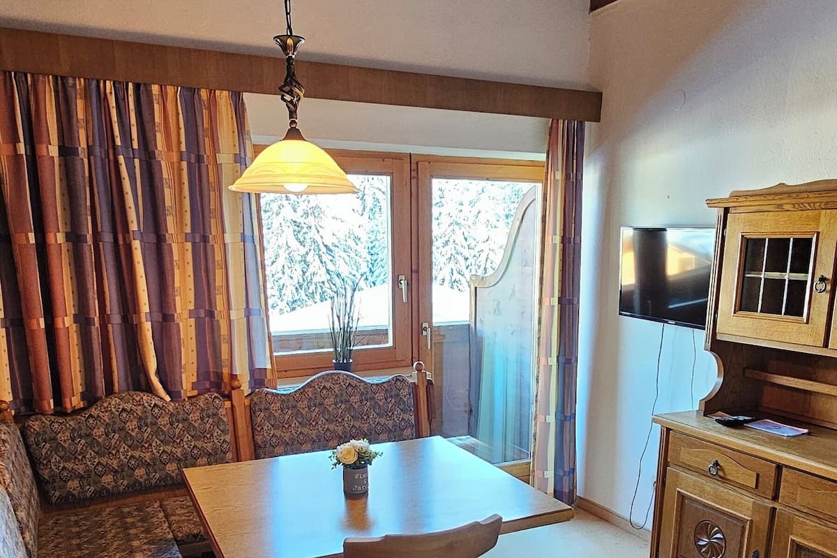 A cozy room with a wooden ceiling, a dining table with chairs, a sofa, a cabinet, and a television.