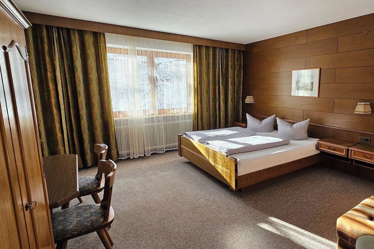 A hotel room with a wooden bed, a desk, a chair, and a sofa.