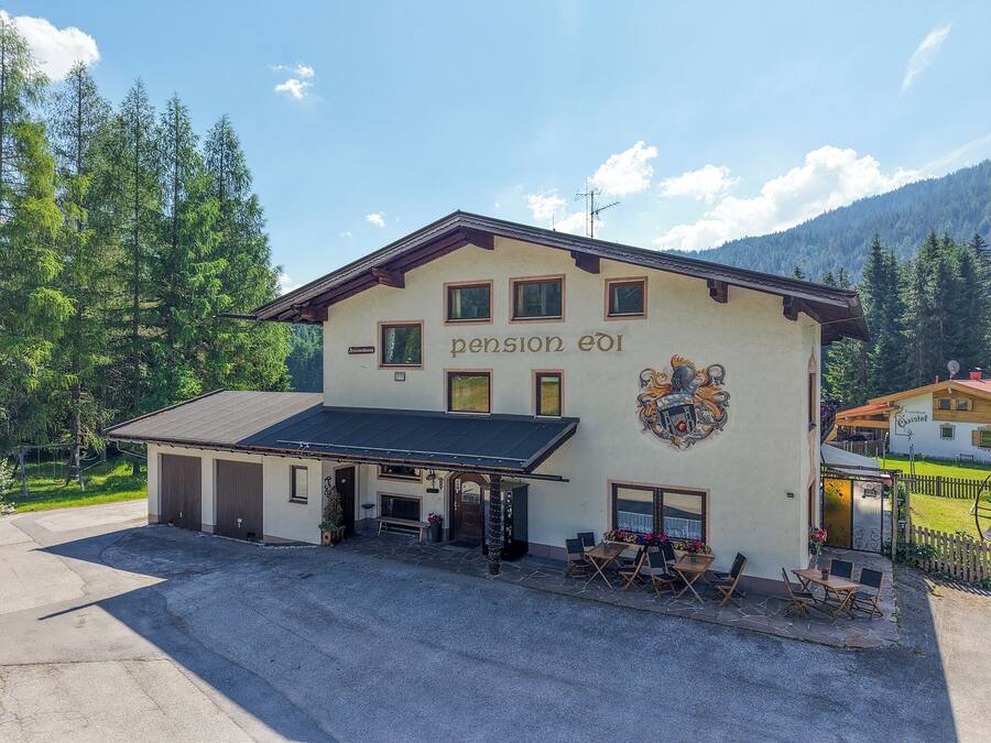 A building with a sign reading 'pension eid' and a coat of arms. There are outdoor tables and chairs, and a covered area with a roof.