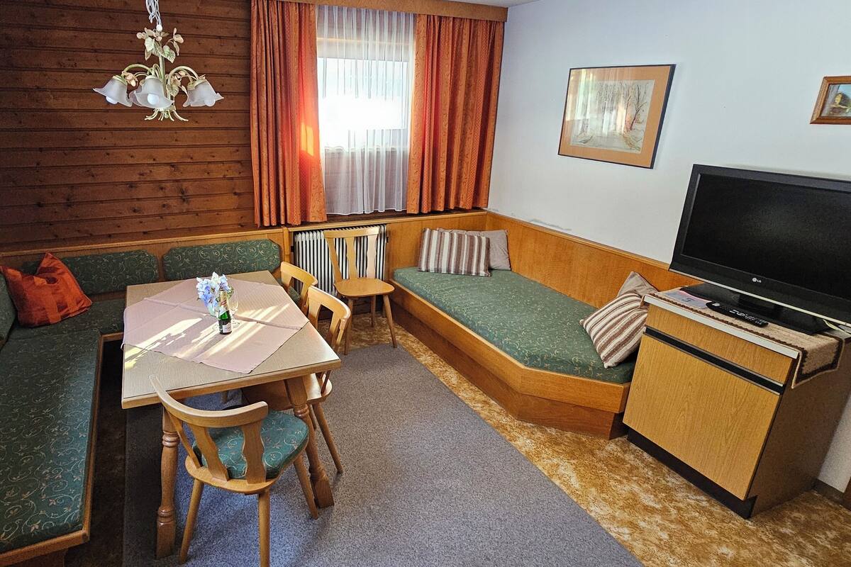 A cozy room with a green sofa, a small table with a bottle, a TV, and a radiator.