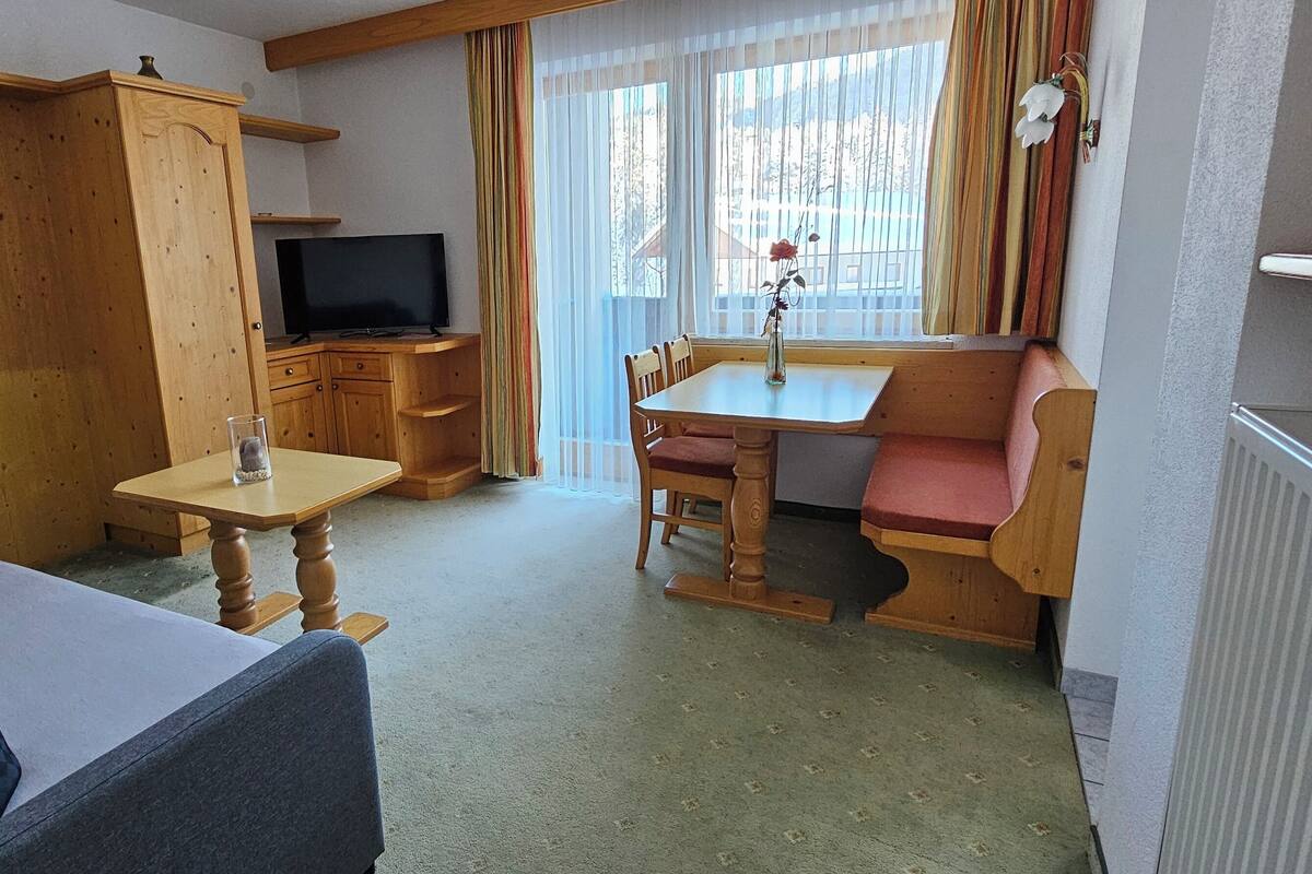 A compact room with a sofa, a small table, a television, and a window with curtains.
