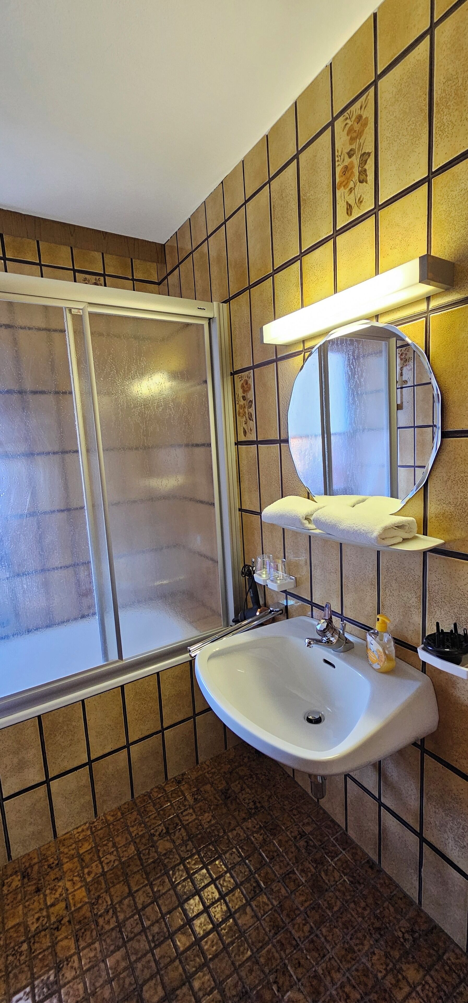 Un bagno con doccia, lavandino, specchio e portasciugamani.