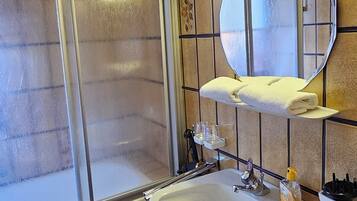 Un bagno con doccia, lavandino, specchio e portasciugamani.