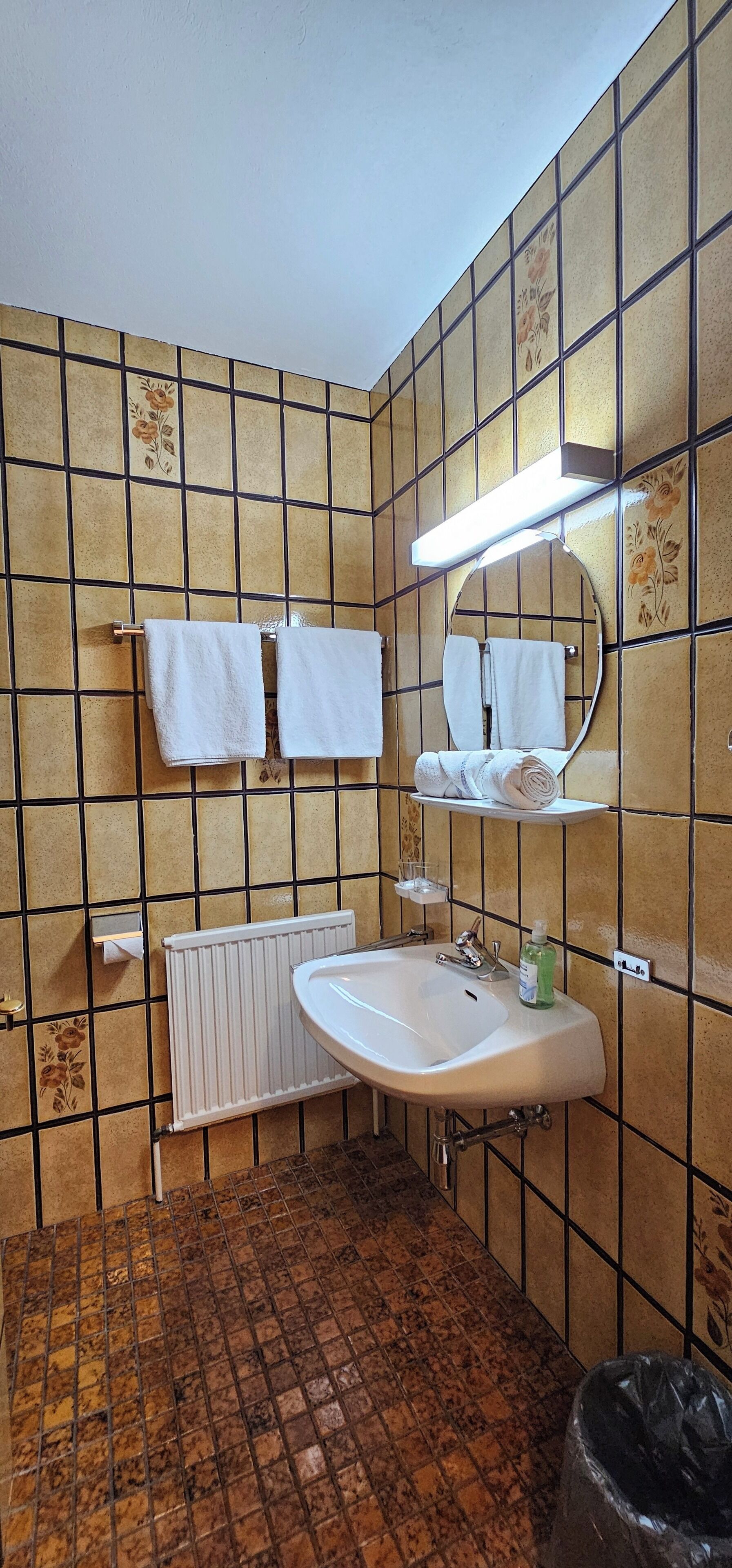 A bathroom with a tiled floor, a sink with a mirror, and two towel racks.