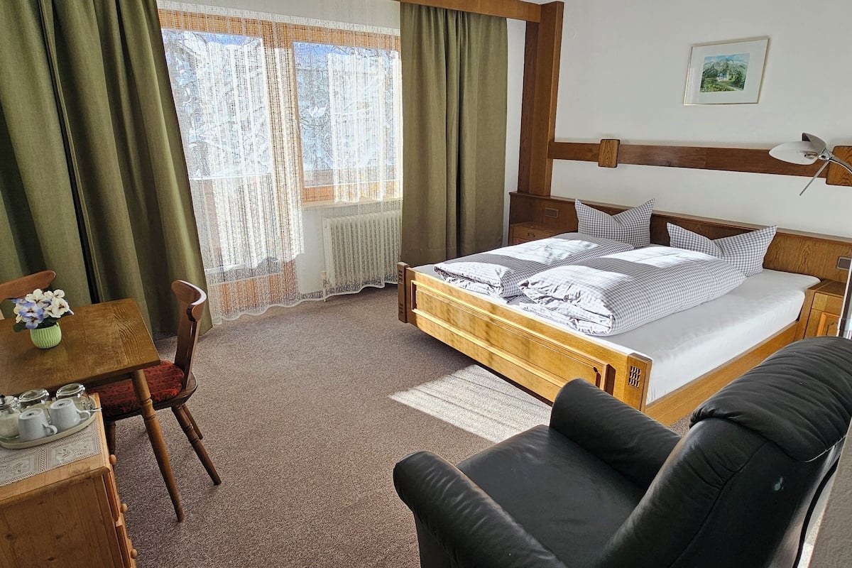 A hotel room with a bed, a desk with a chair, a TV, and a window with curtains.