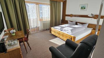 Habitación de hotel con cama, escritorio, silla, televisor y ventana con cortinas.