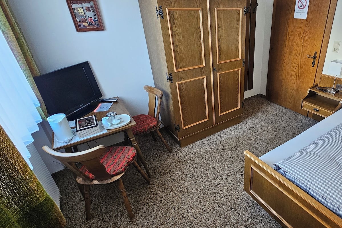 A compact bedroom with a bed, a desk with a computer, a chair, and a wardrobe.