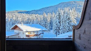 A room with a large window overlooking a snowy landscape and a building. - Pension Edi (Leutasch)