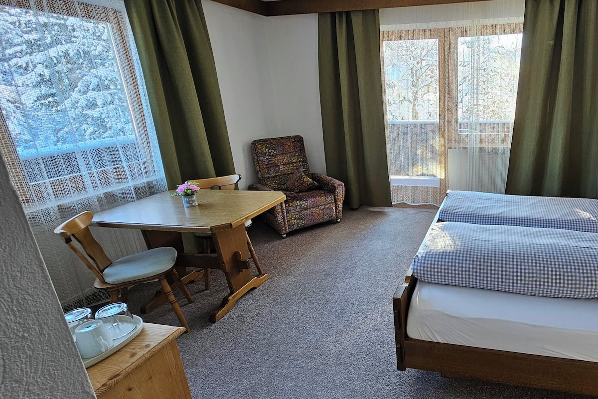 A room with a bed, a chair, a table, and a window with curtains.